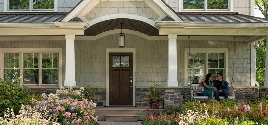 couple sitting outside on a patio swing next to a well maintained entry door