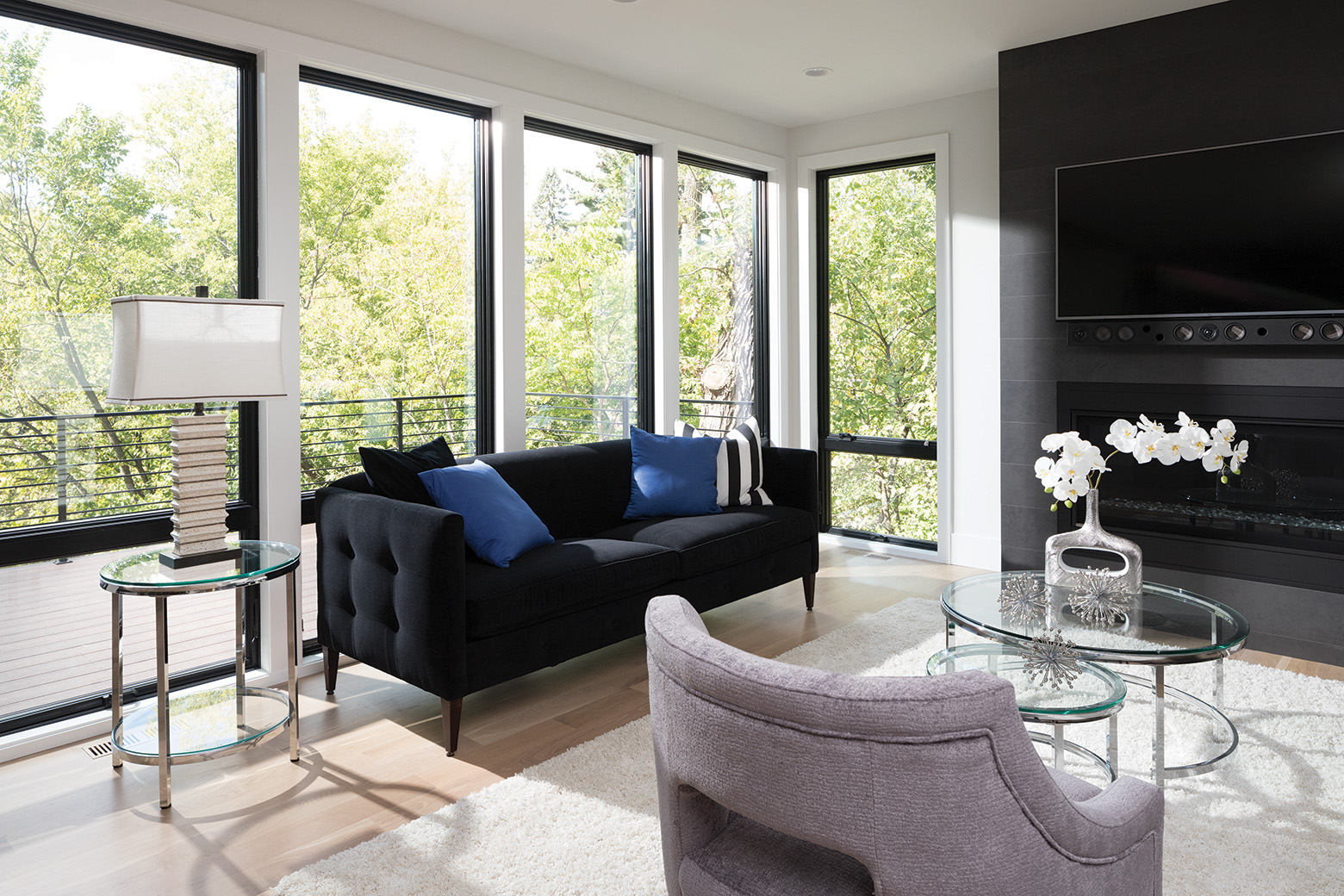 a living room with wood floors and white walls and a dark blue couch with a large electric fireplace beneath a flatscreen tv