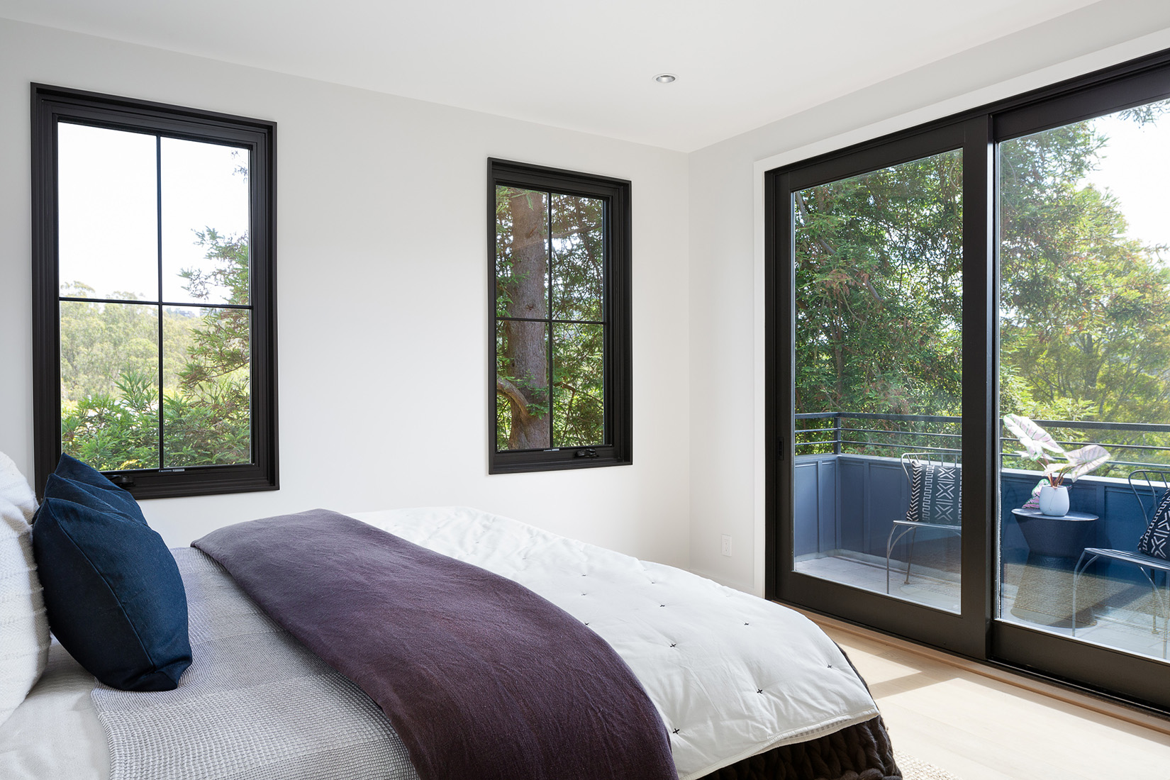 Comfortable bed beside 2 windows and a sliding balcony door