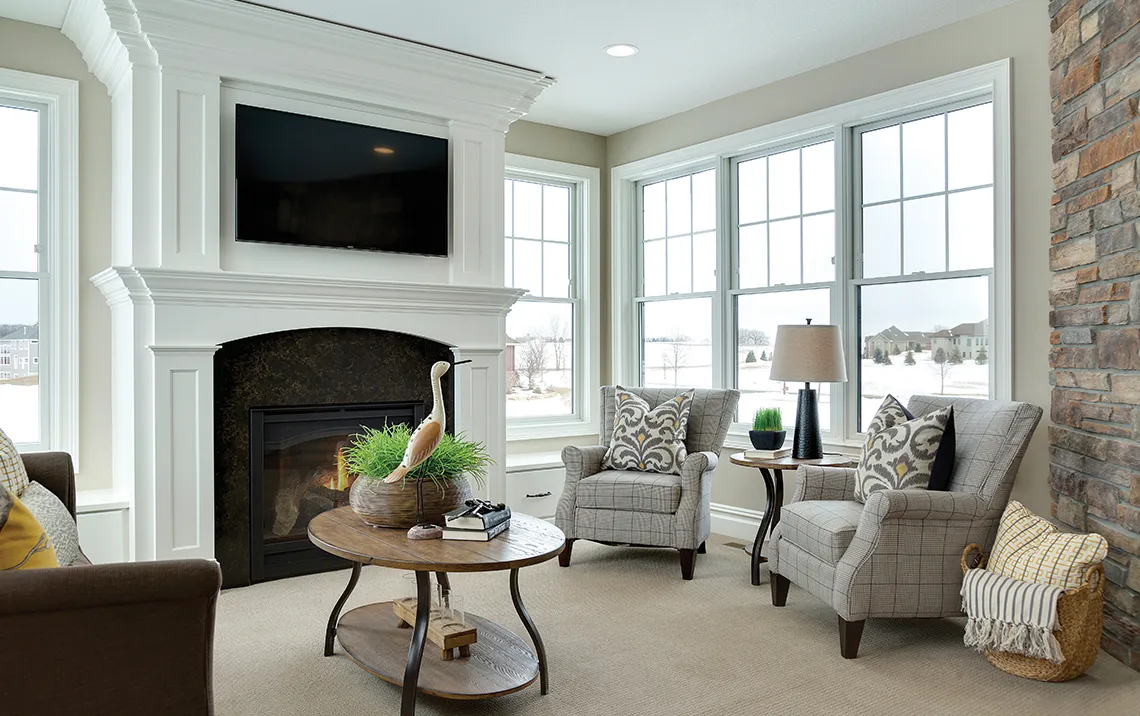 a modern living room with an electric fireplace and comfortable chairs and a couch beside it with windows letting in natural light