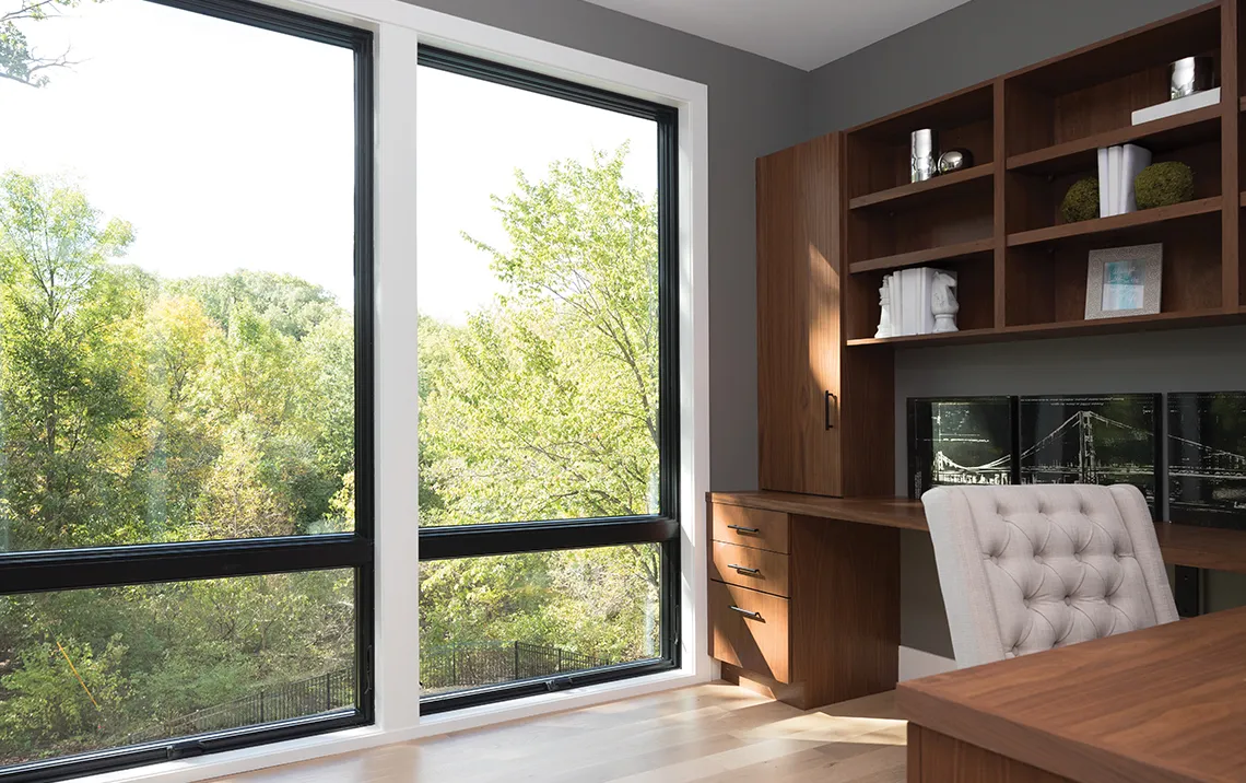 an office space with wooden desk and cabinets with full wall size glass windows looking at tree tops