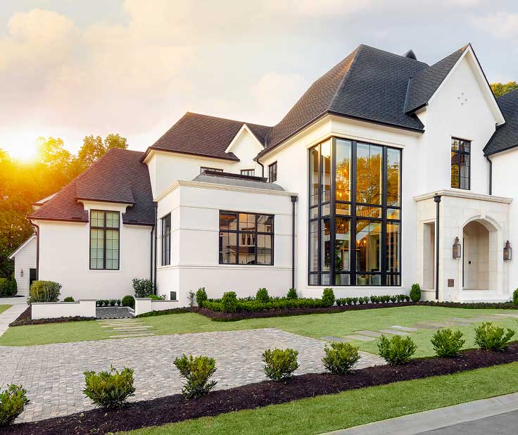 white home exterior with large windows and sun setting over trees behind the house