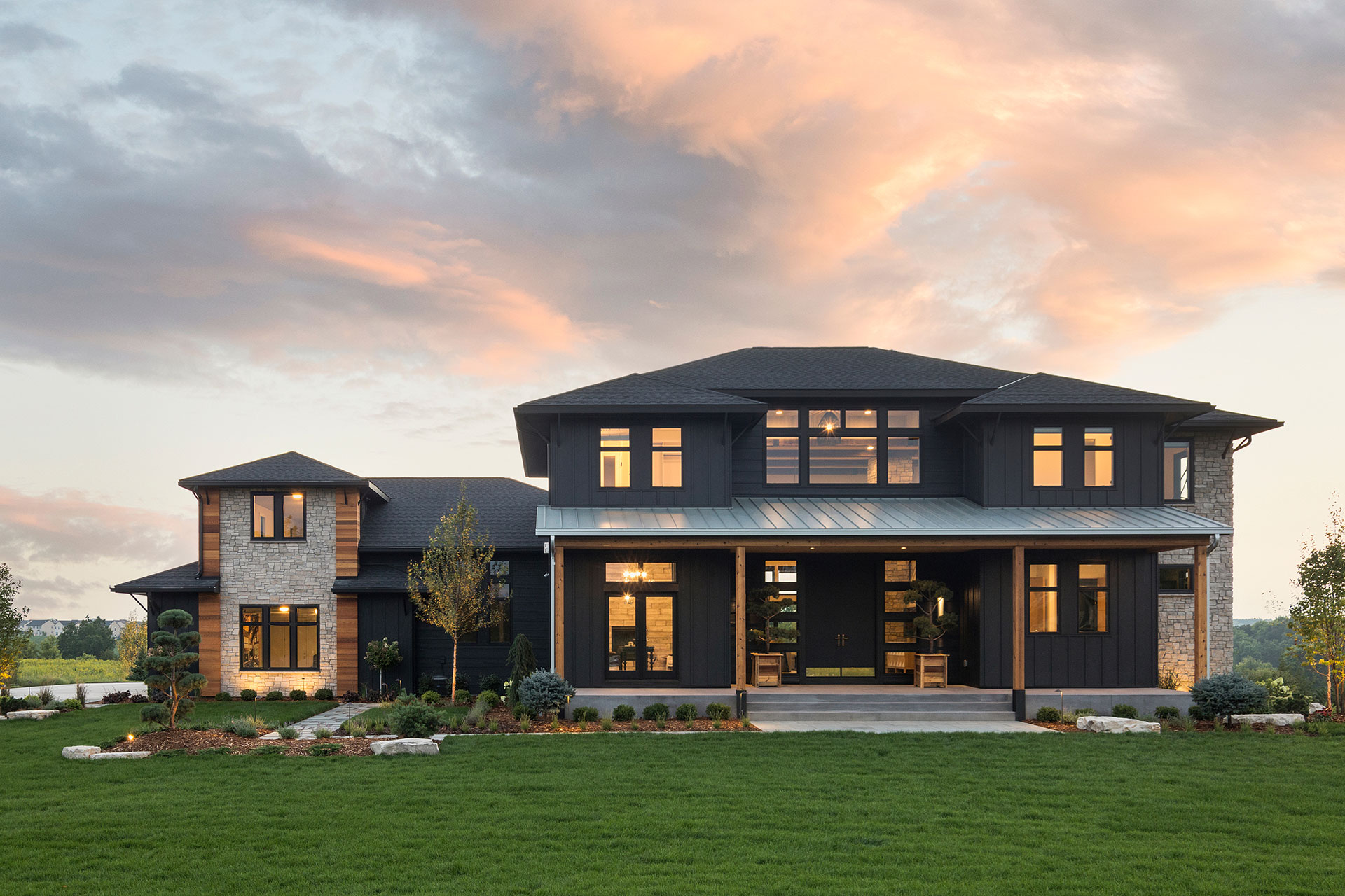 home exterior featuring dark gray walls with brown accents with warm lighting inside large glass windows